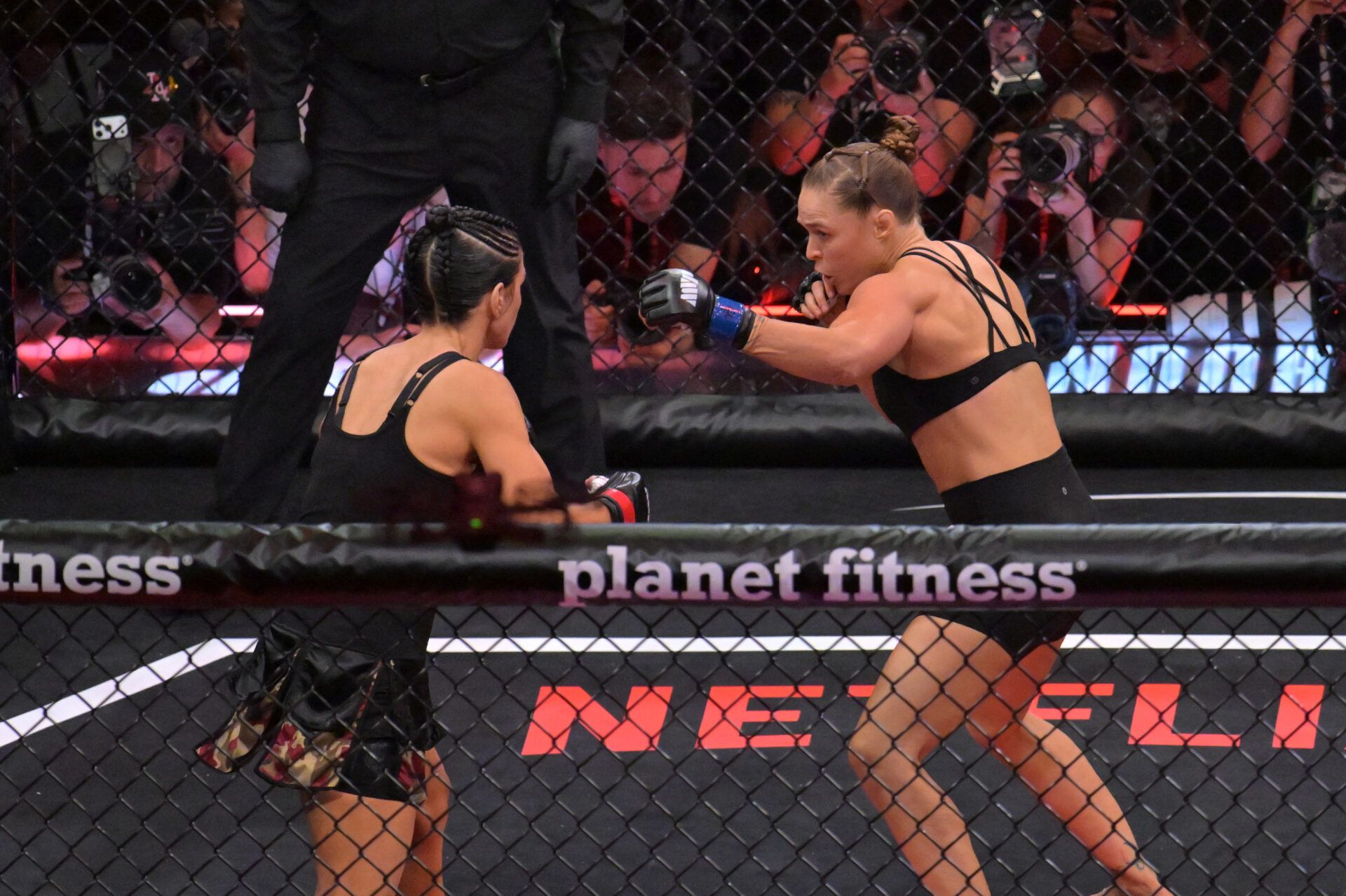 Ronda Rousey (blue gloves) fights Gina Carano (red gloves) in a women's featherweight bout at Intuit Dome.