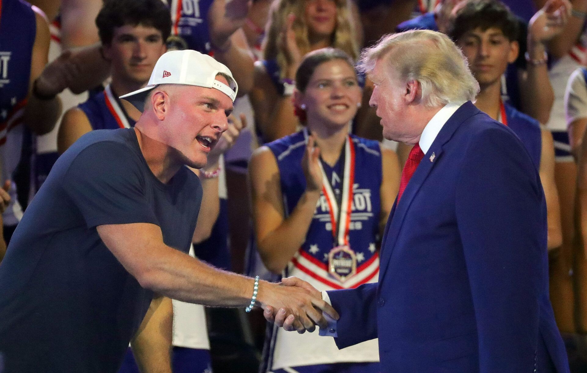 ESPN personality Pat McAfee, left, shakes hands with President Donald Trump during the Patriot Games held at Spire Academy, Aug. 11, 2026, in Geneva, Ohio.